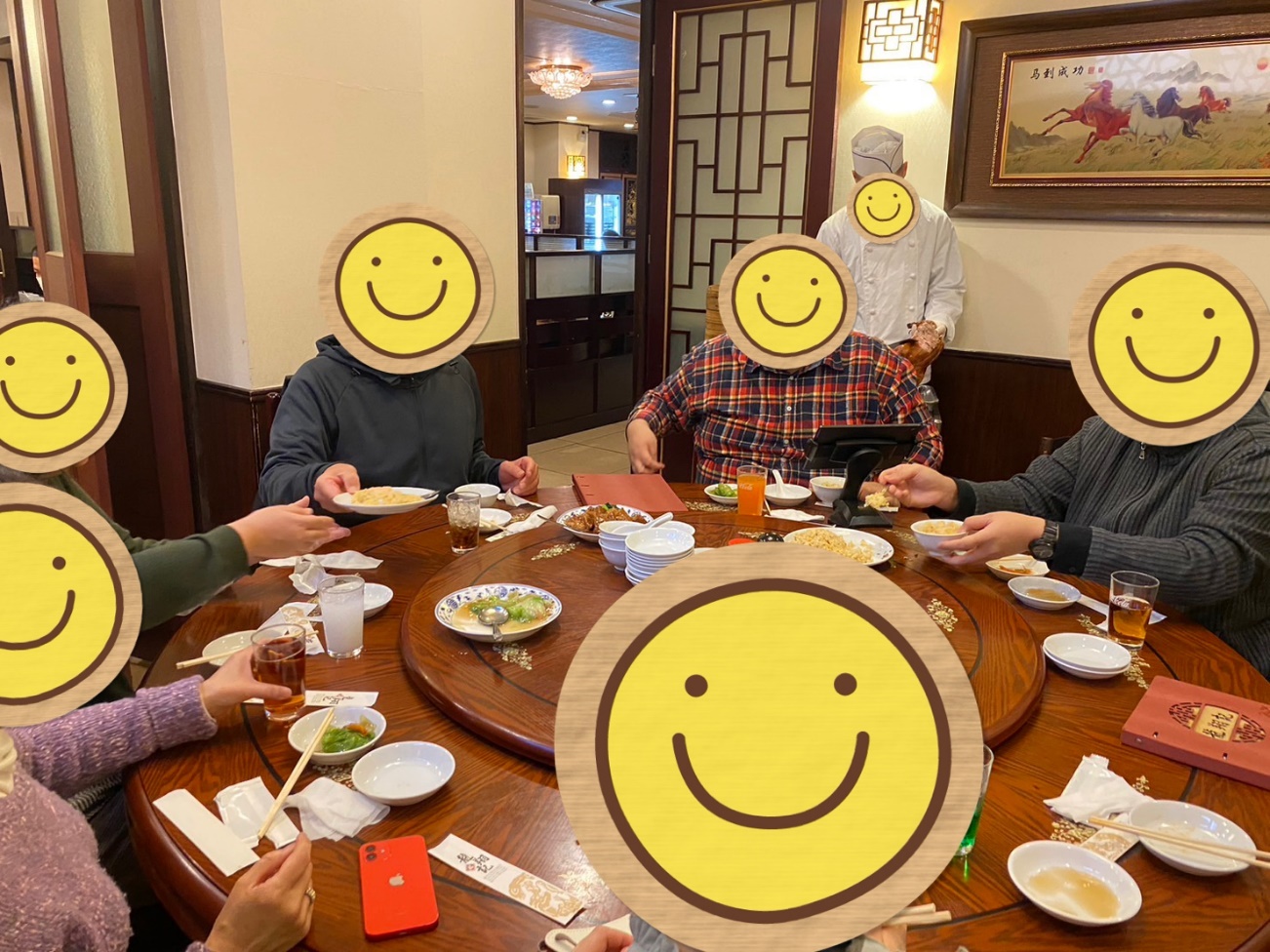 料理人が北京ダックを切り分けるパフォーマンスを行っている横で、参加者6名が楽しげに中華料理を食べる光景の写真