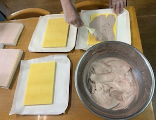 泡立てたチョコレート生クリームをケーキのスポンジ生地に塗っています。