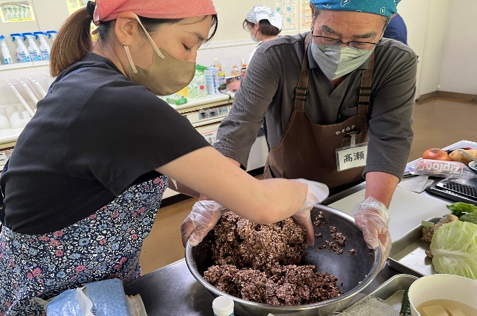 男性がボウルを押さえ、女性が木べらで味噌を混ぜています。