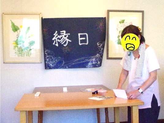 一人のメンバーが交流会の準備をしています。壁には「縁日」と書かれた旗が、その両隣には花と草が描かれた絵画が飾られています。