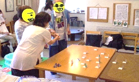 三人で一緒に射的をしています。一人がピストルに輪ゴムをうまく引っ掛けられず、そのうちの二人がサポートしています。
