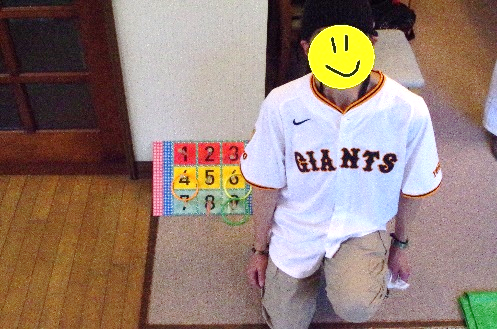 一人のメンバーが輪投げを投げ終わり、ボードを背にしてしゃがんで、記念撮影を撮っています。