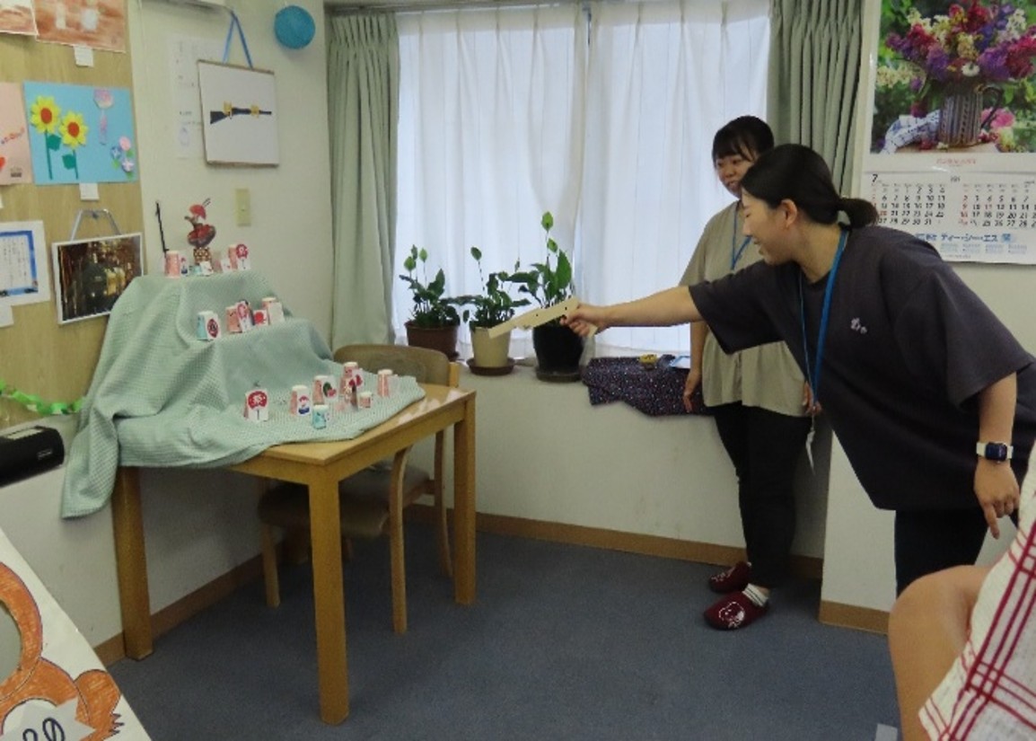 職員が射的ゲームで、鉄砲を構えて的を狙っています。
