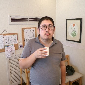コップを手に持ち、カメラの方を見る男性。