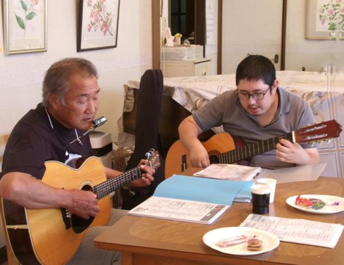 アコースティックギターを持つ2人。うち1人はハーモニカを使用して演奏する。
