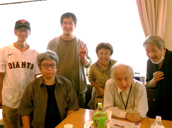 参加者の一部と並んで記念撮影をしている場面。