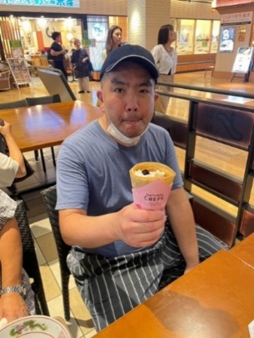帽子をかぶった男性が、デザートのクレープを食べています。